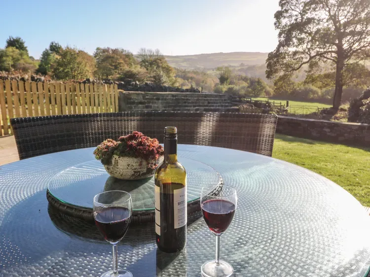 Una mesa de patio con copas de vino da a un paisaje rural verde.