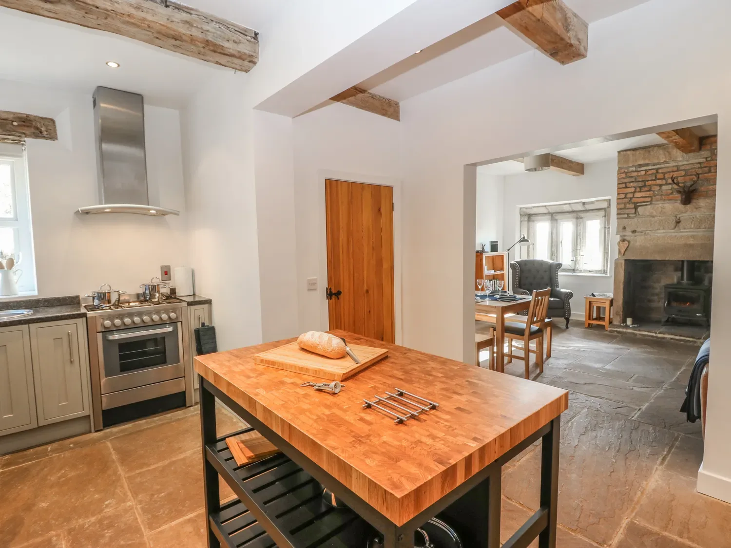 A kitchen with a wooden island, stainless steel oven, and a view into a dining area with a fireplace at The Cottage Beeston Hall in Ripponden