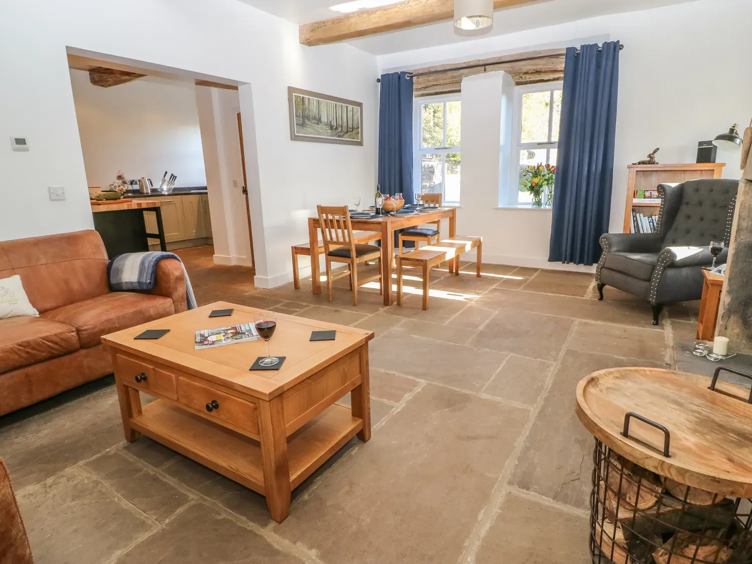 A living room with a brown sofa wooden coffee table dining table with chairs blue curtains and a gray armchair at The Cottage Beeston Hall Ripponden