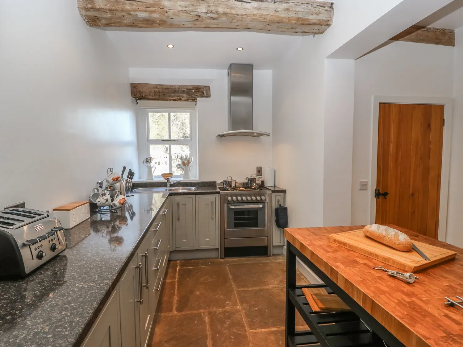 A kitchen with a long counter and a wooden worktable holding a loaf of bread.