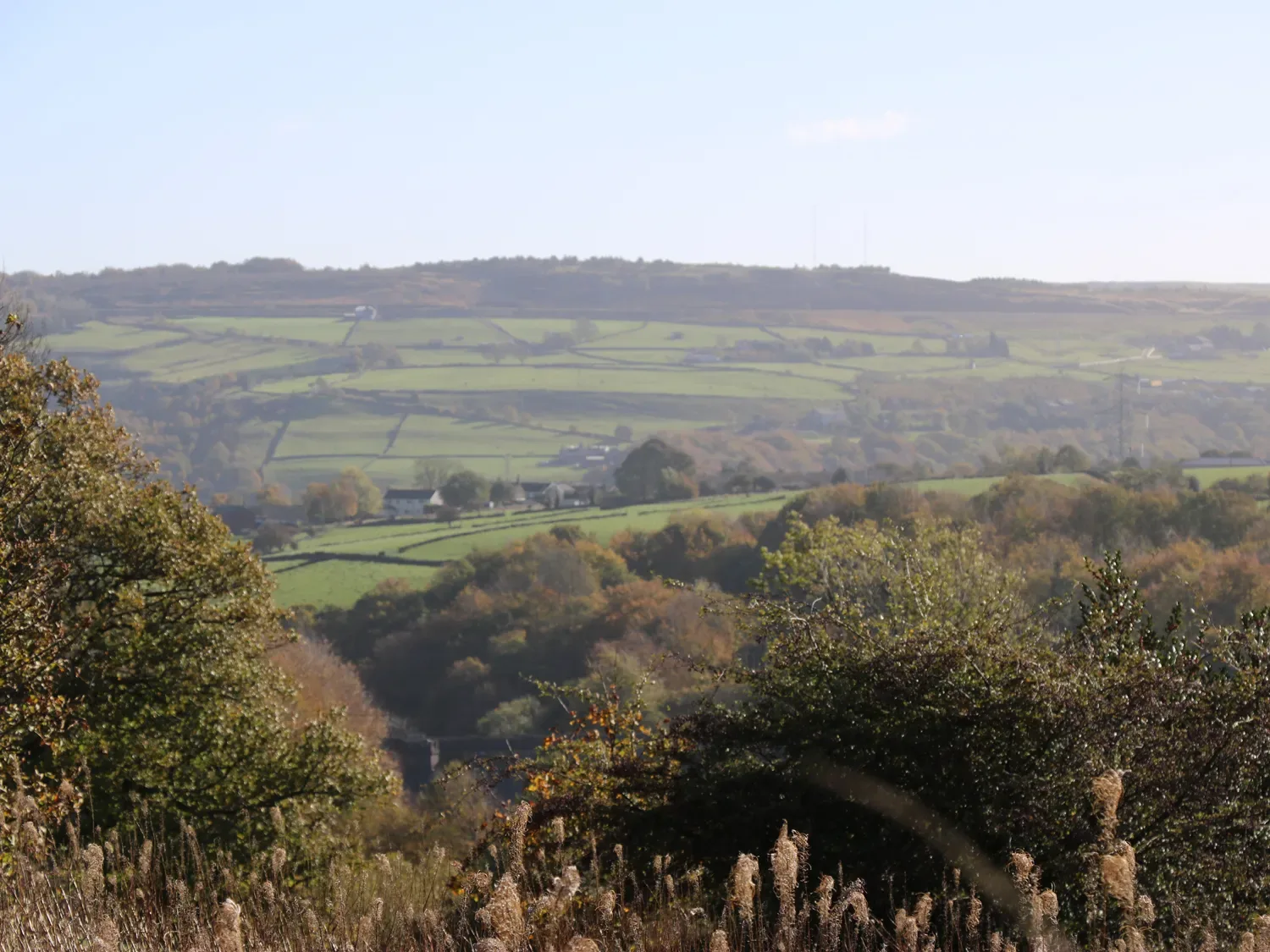 A rural landscape of green fields, wooded slopes, and distant hills.
