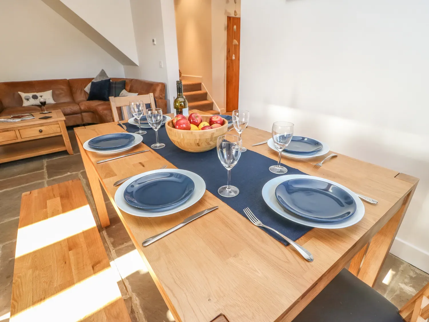 A dining table set with plates glasses and cutlery and a bowl of fruit next to a living area with a sofa and coffee table at The Cottage Beeston Hall in Ripponden
