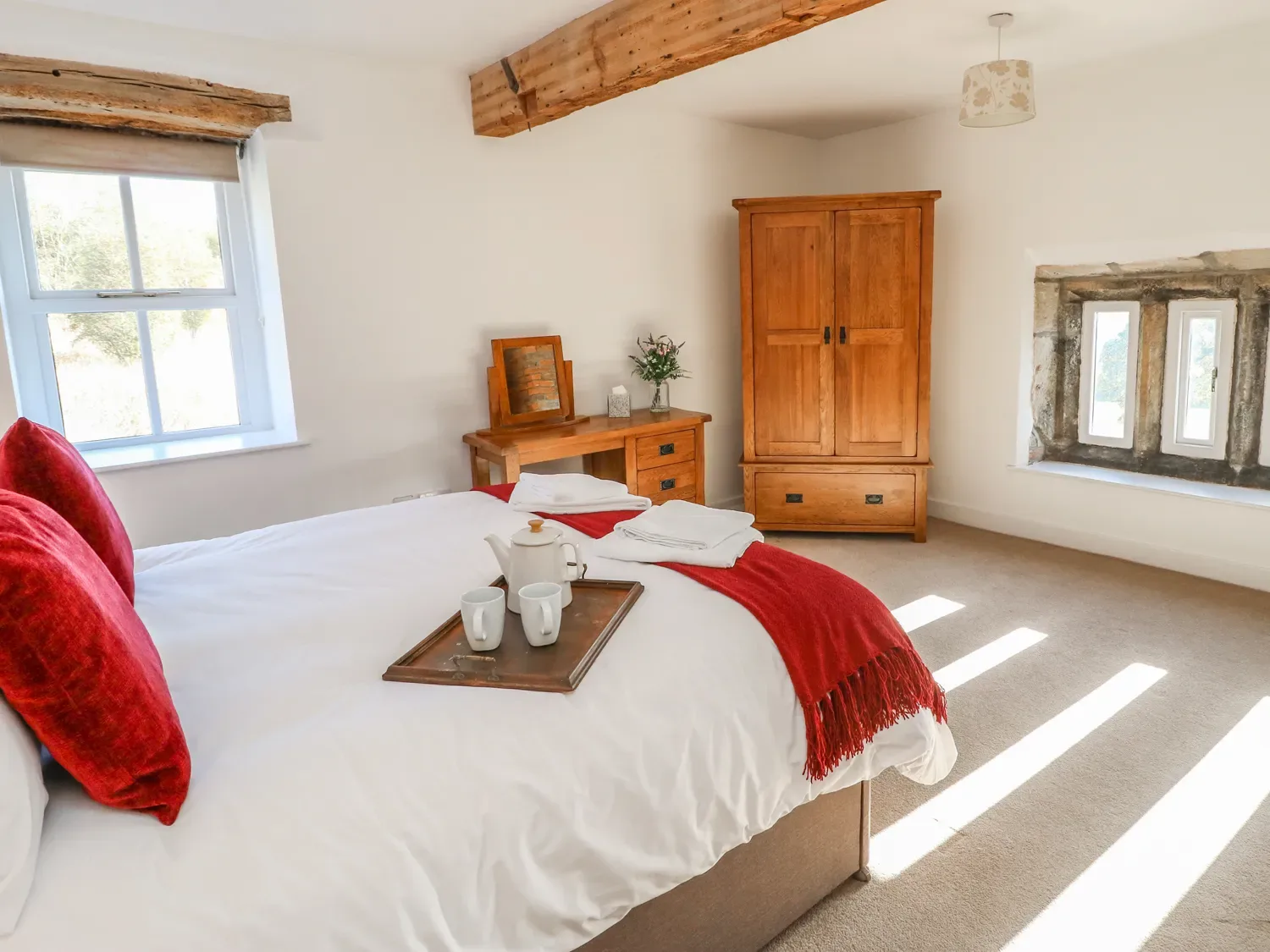 A bedroom with a bed with red pillows and throw a wooden wardrobe and dressing table with a mirror at The Cottage Beeston Hall in Ripponden