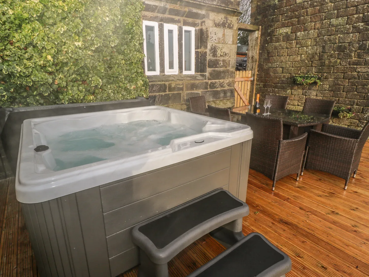 An outdoor patio features a hot tub beside a dining table and seating.