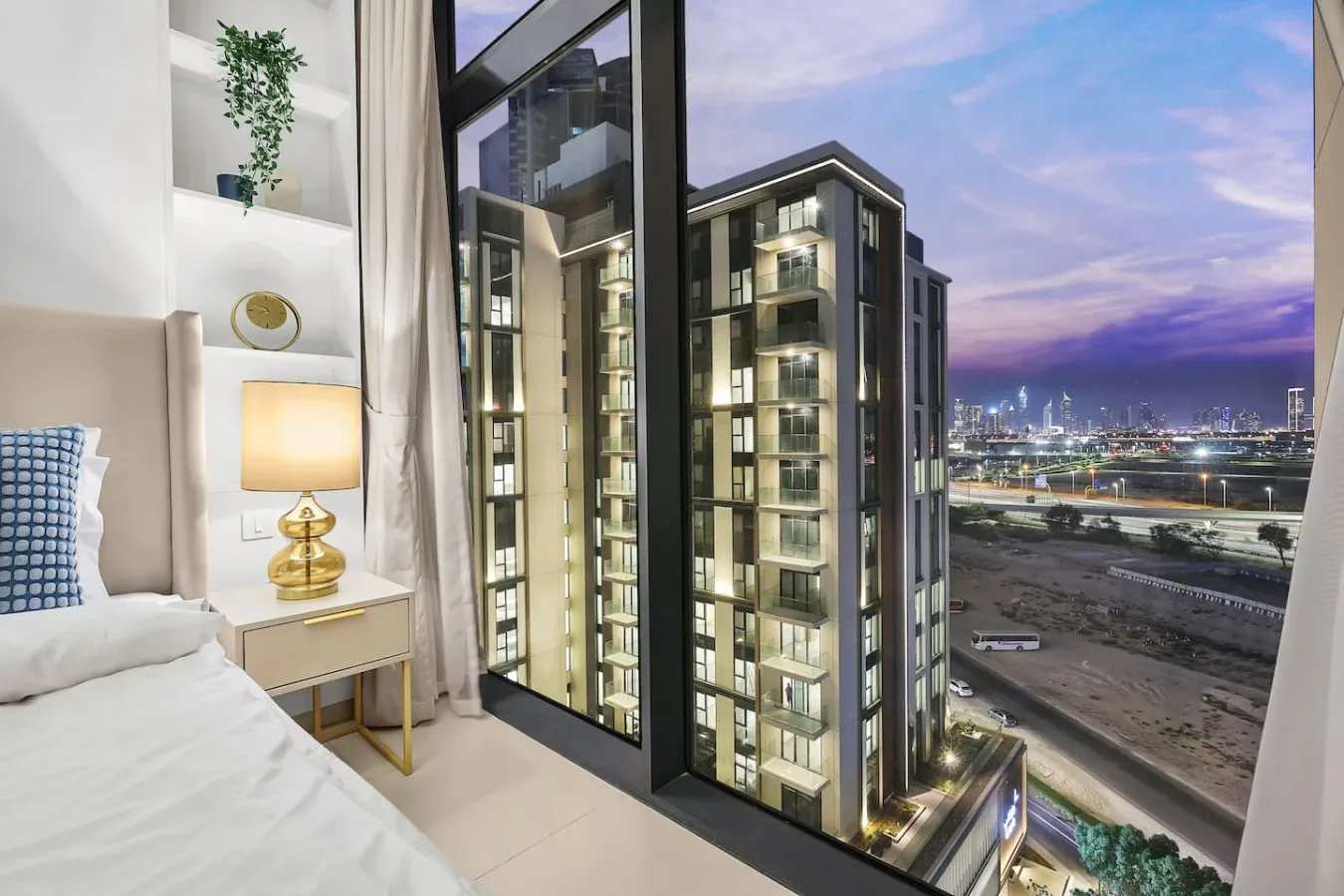 Dormitorio con una gran ventana con vistas a edificios iluminados y luces de la ciudad.