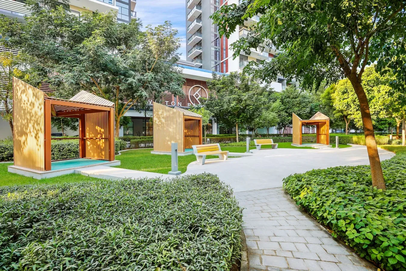 Un patio ajardinado con senderos pavimentados, bancos y estructuras de madera con sombra.