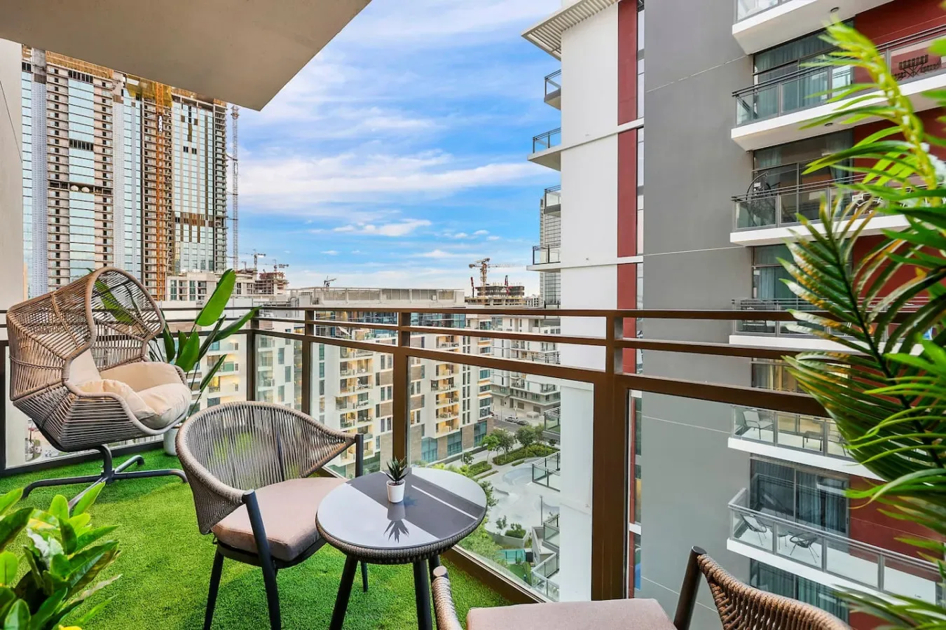 Un balcón amueblado con asientos y plantas en macetas da a edificios de apartamentos cercanos.