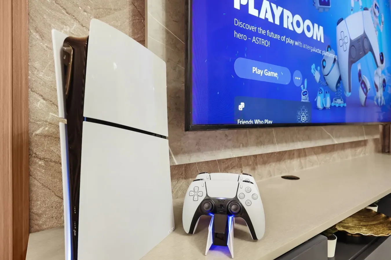 Una consola de videojuegos y un mando están sobre un estante bajo un televisor montado en la pared.