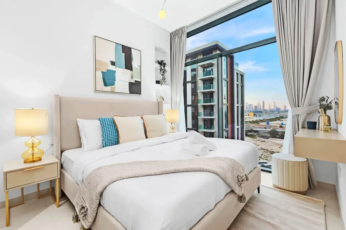 Un dormitorio luminoso con una cama bien tendida junto a una gran ventana con edificios a la vista.