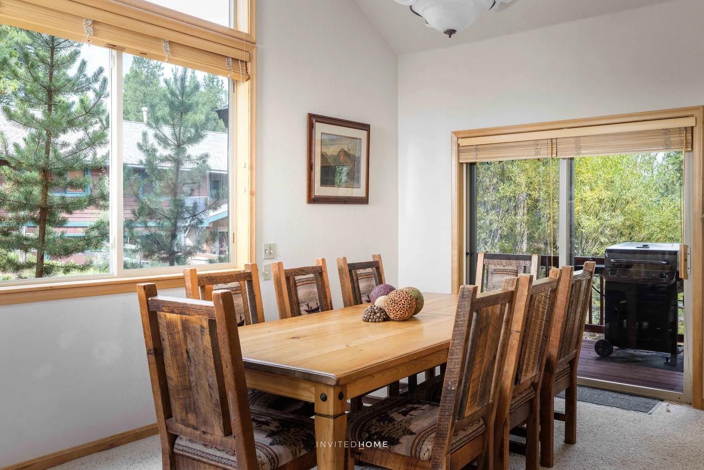A dining area with a wooden table and chairs beside large windows.