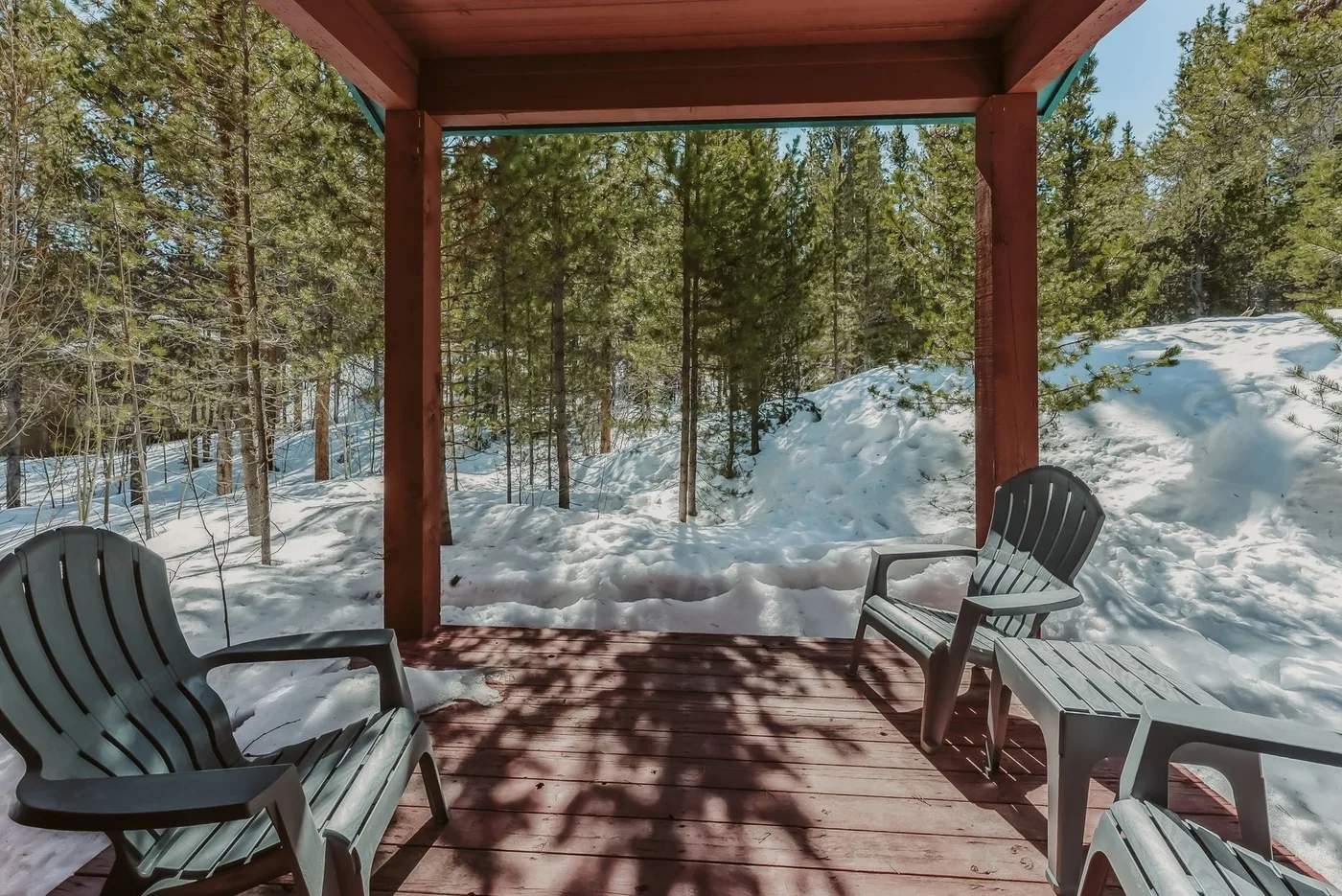 A wooden porch with seating overlooks a snowy landscape and trees.