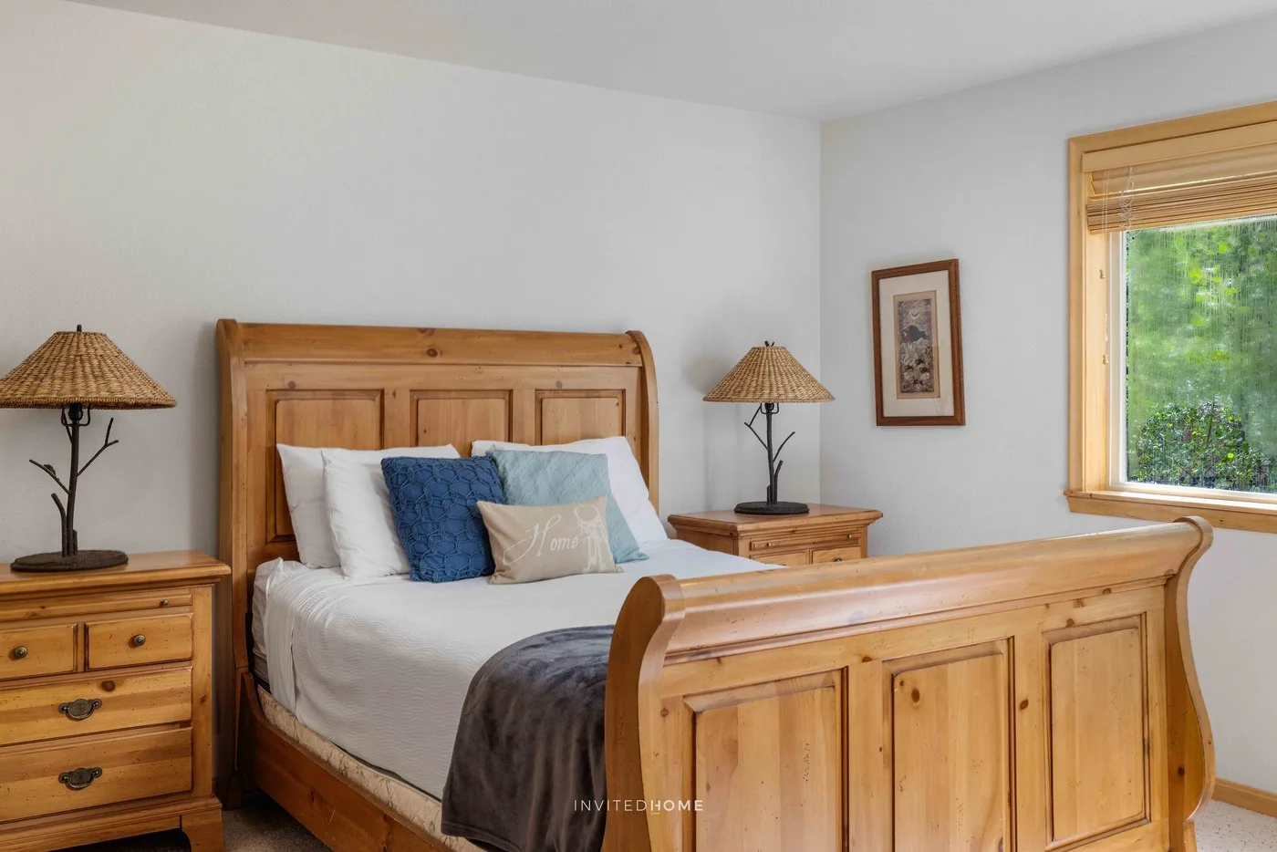 A bedroom with a wooden bed, bedside tables, and a window overlooking greenery.