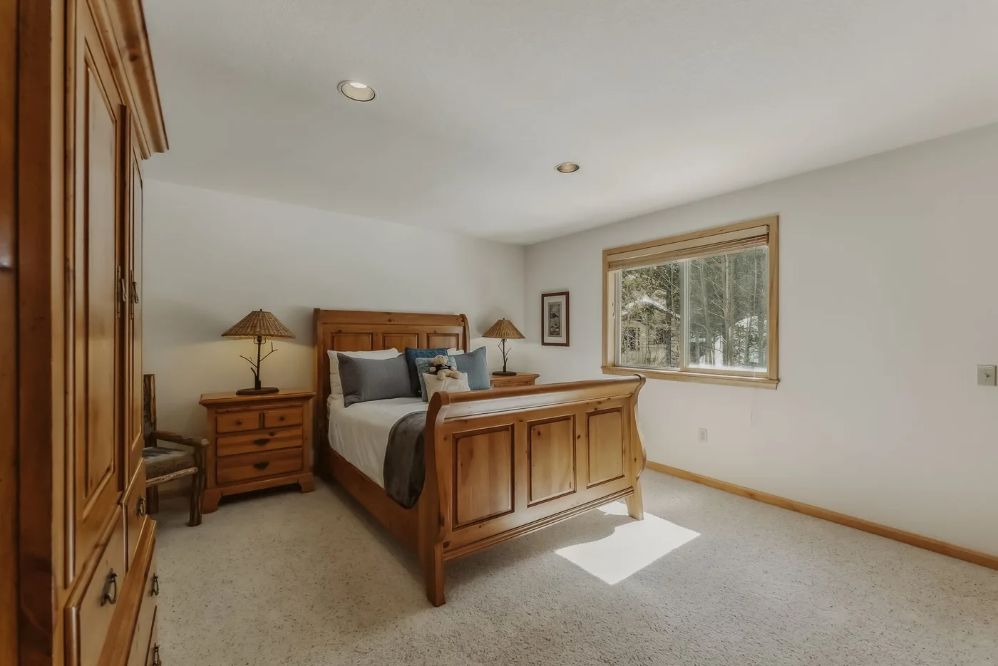 A bedroom with a wooden bed and a large window overlooking trees.