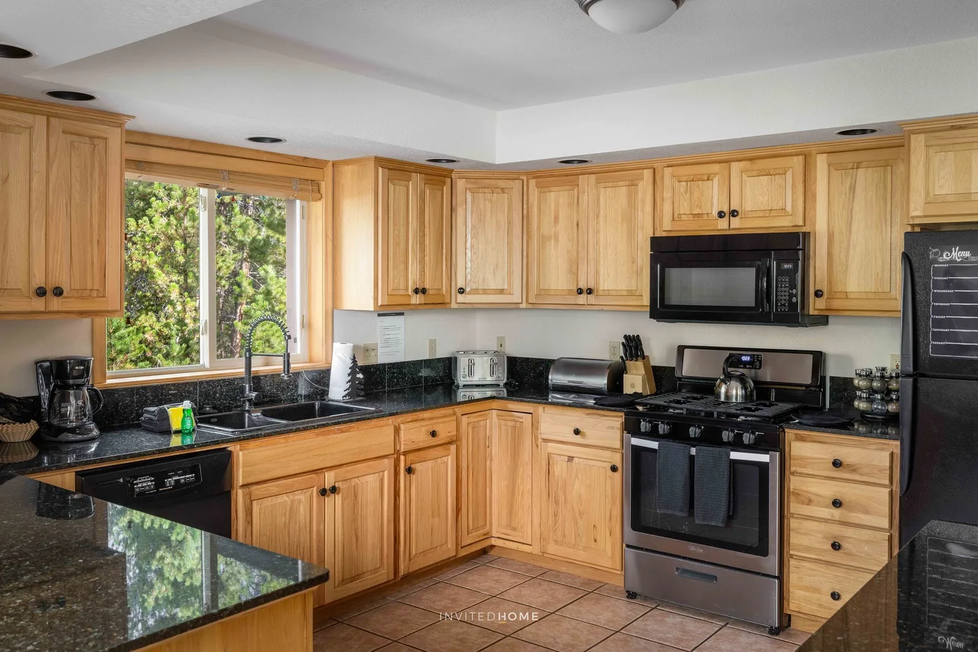 A kitchen with wooden cabinets, dark countertops, and a range.