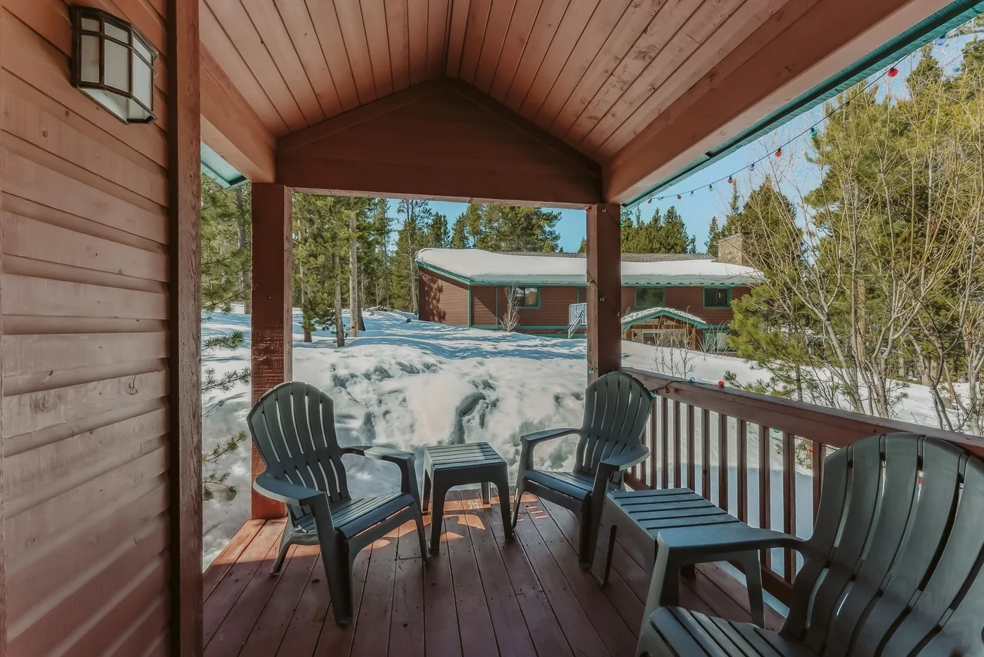A covered wooden porch overlooks a snowy landscape and nearby buildings.