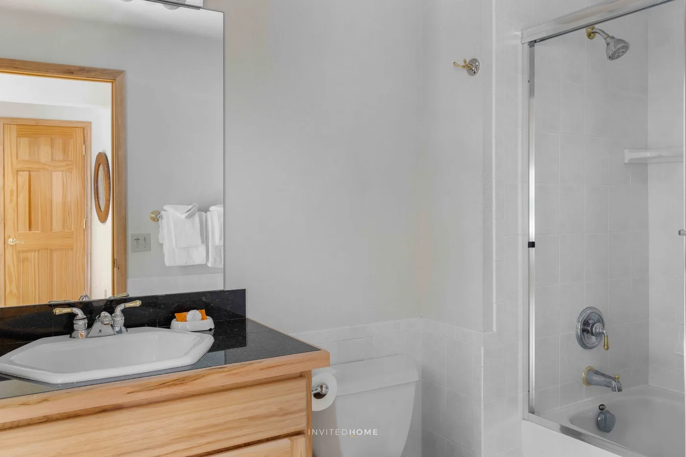 A bright bathroom with a vanity, sink, toilet, and glass-enclosed shower.