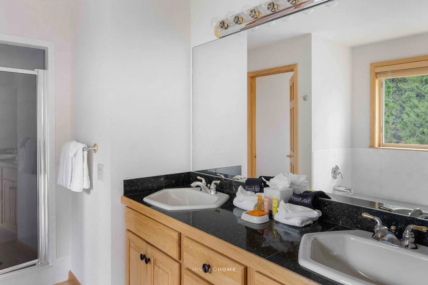 A bathroom vanity with two sinks, a large mirror, and a window.