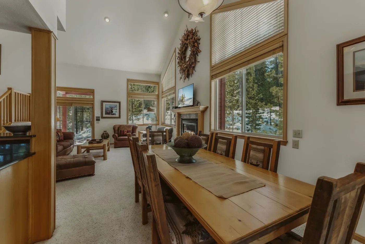 A dining area with a long wooden table beside a living room and large windows.