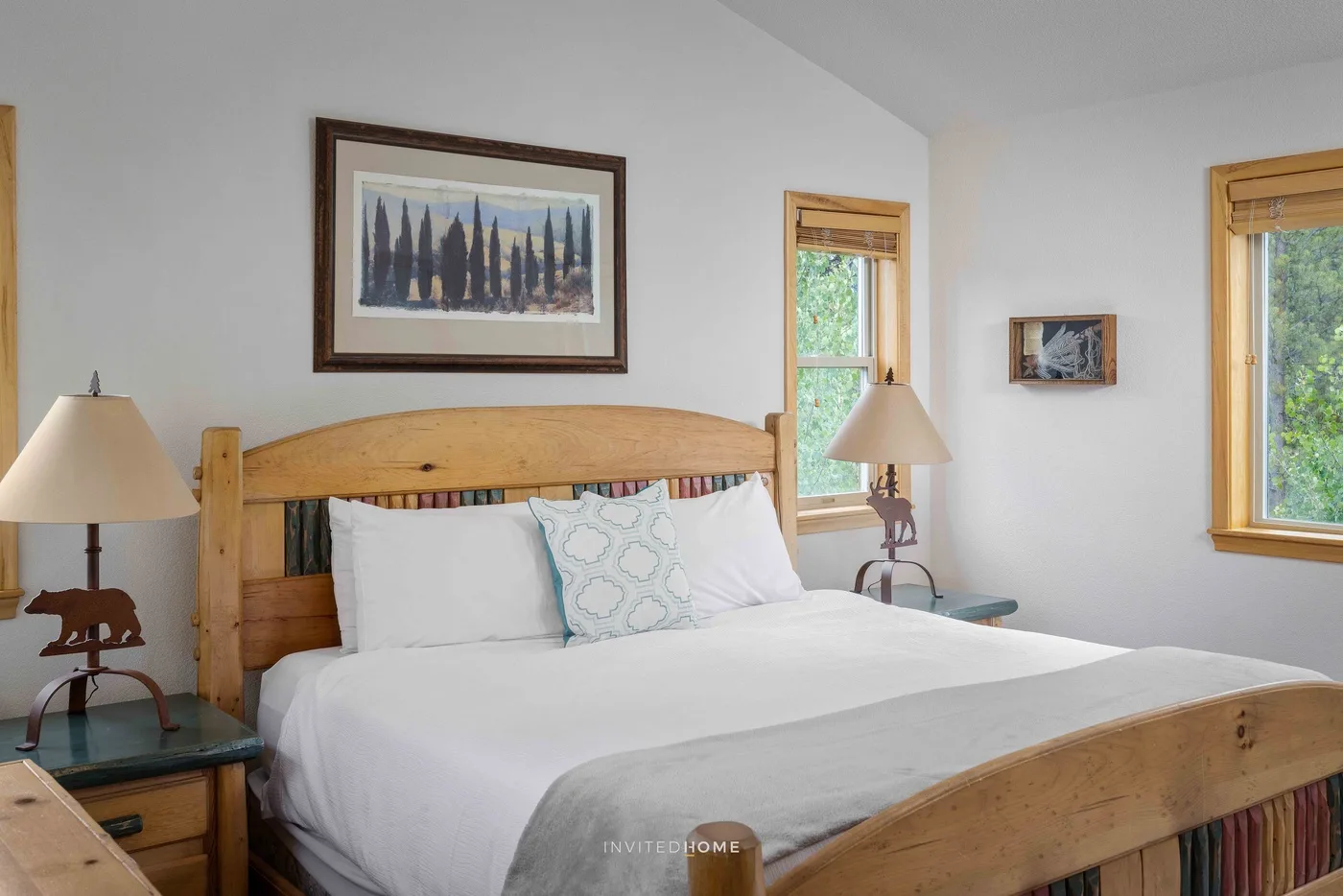 A bedroom with a wooden bed, white bedding, and framed artwork above it.