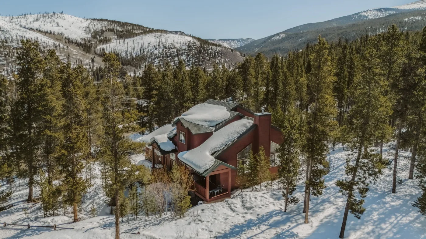 A red lodge sits among snow-covered trees in a mountain landscape.