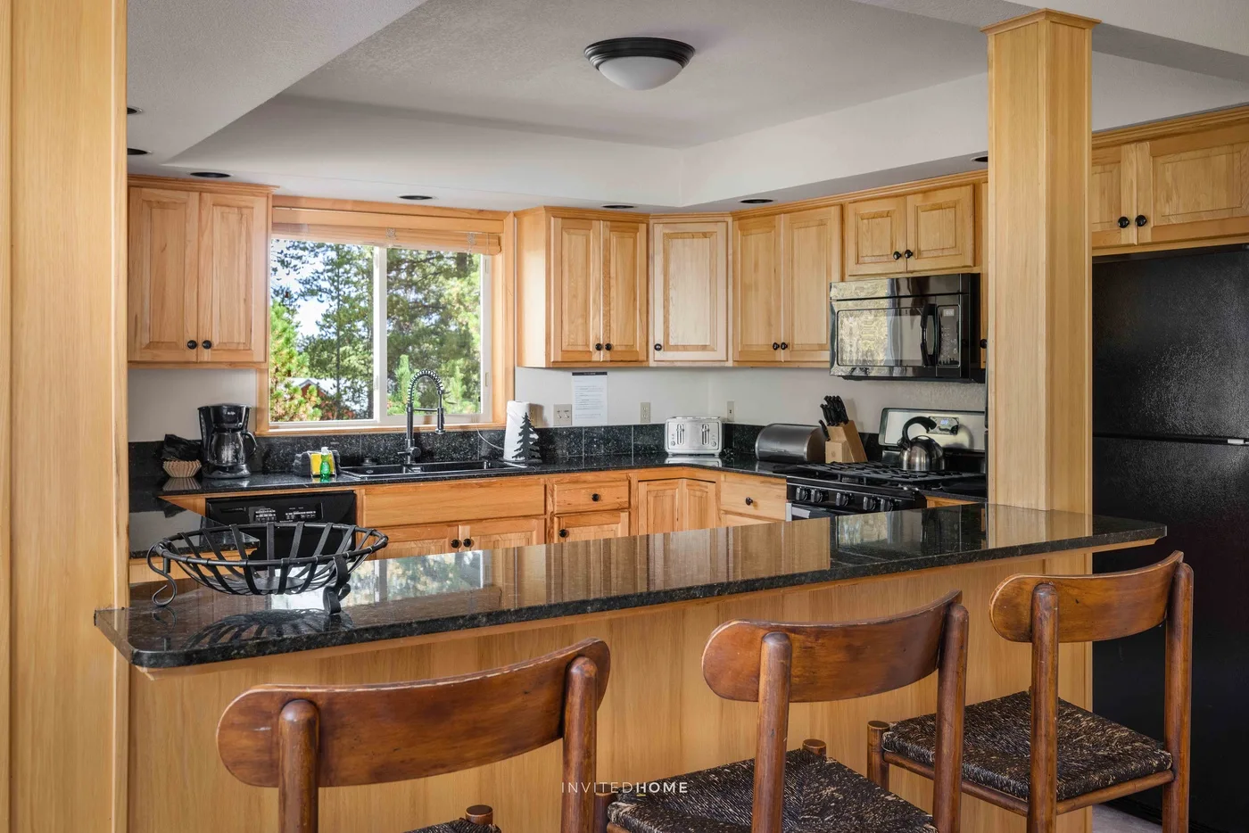 A bright kitchen with wooden cabinets, dark countertops, and a breakfast bar.