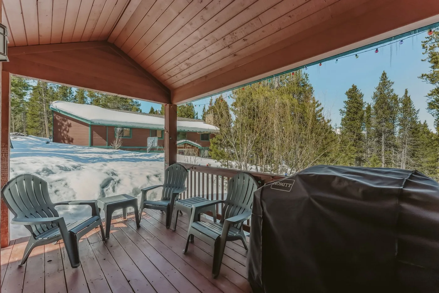 A covered deck with outdoor seating and a covered grill overlooks a snowy landscape.