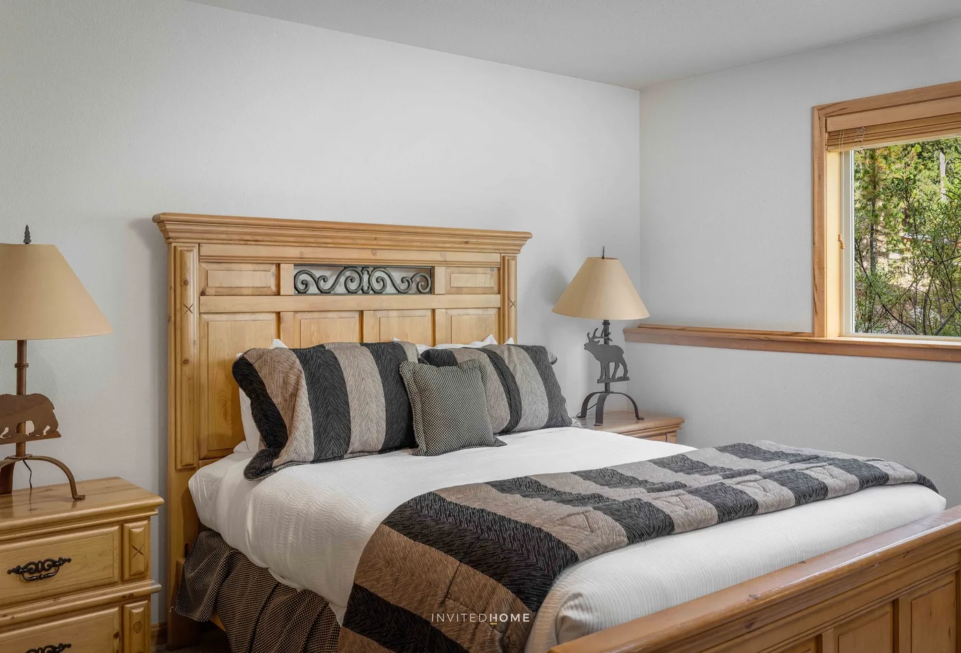 A bedroom with a wooden bed, striped bedding, and a window overlooking greenery.