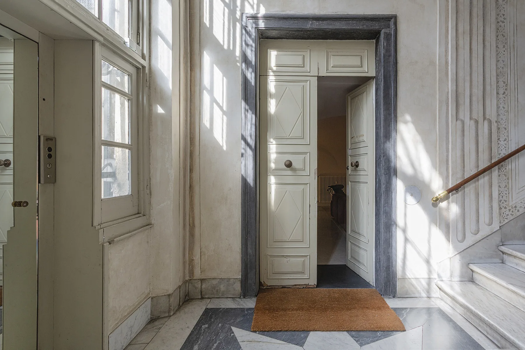 Un vestíbulo luminoso con ventanas altas, una puerta y escaleras.