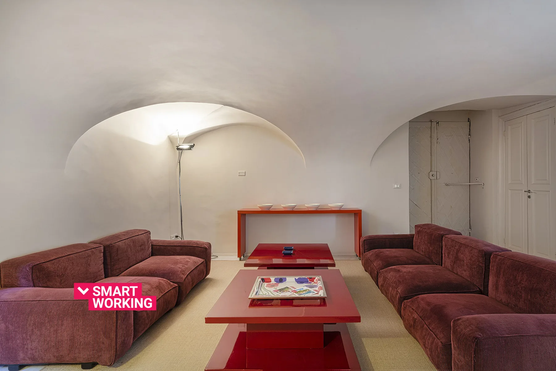 Una sala de estar con asientos color burdeos, una mesa de centro roja y una lámpara de pie.