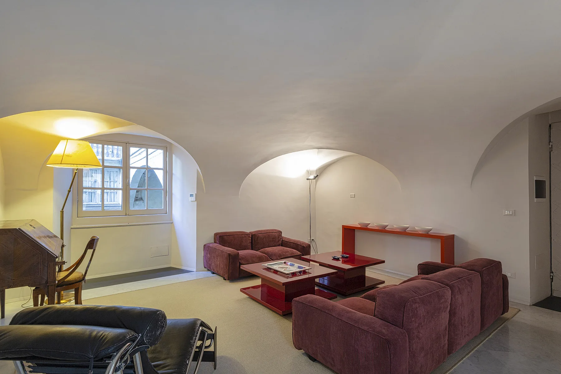 Una sala de estar con asientos color burdeos, una mesa de centro y arcos.