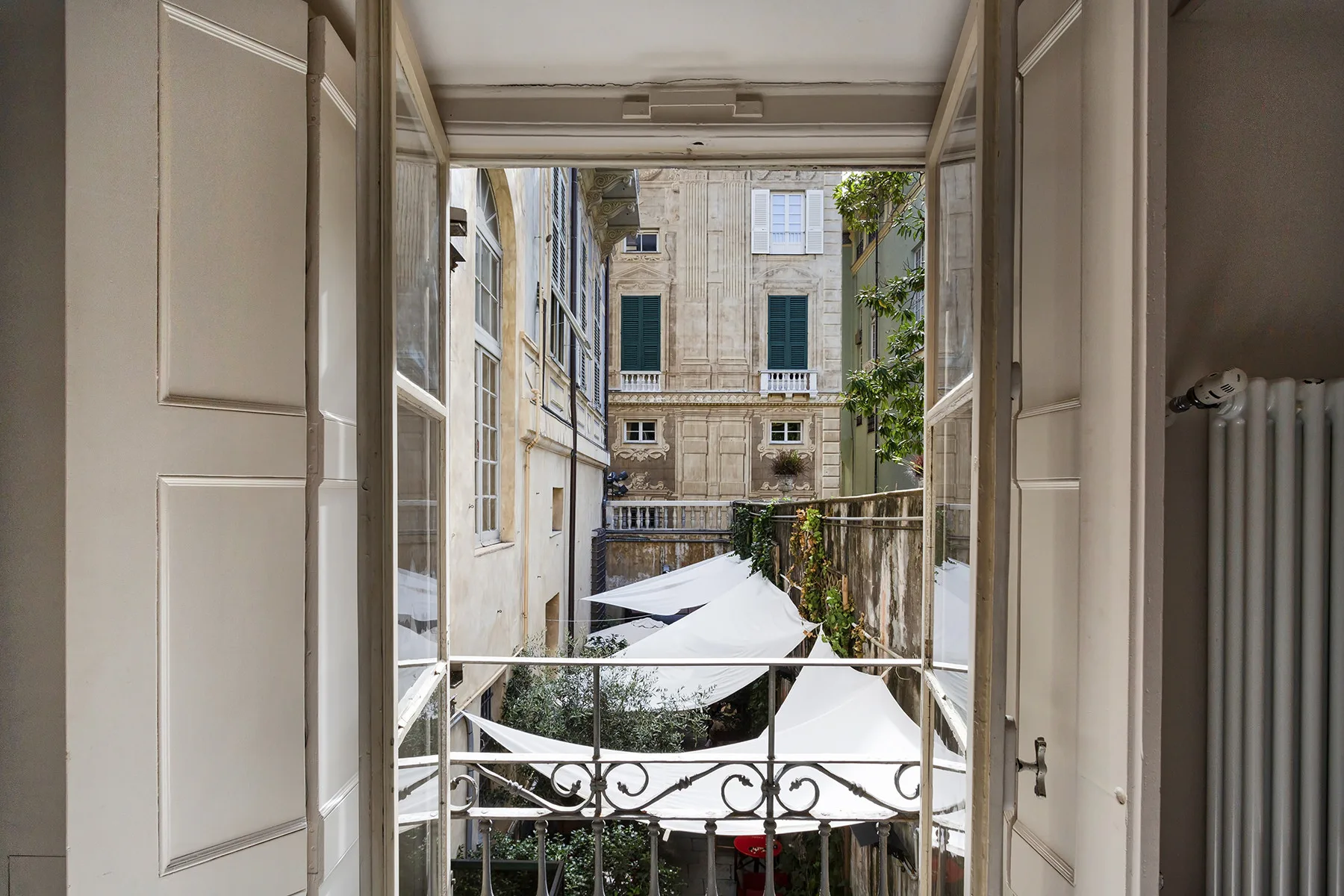 Una puerta abierta da a un patio con toldos blancos y edificios alrededor.