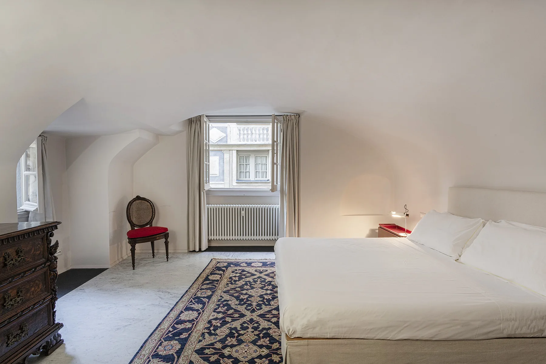 Un dormitorio con una cama grande, una alfombra estampada y ventanas bajo un techo inclinado.