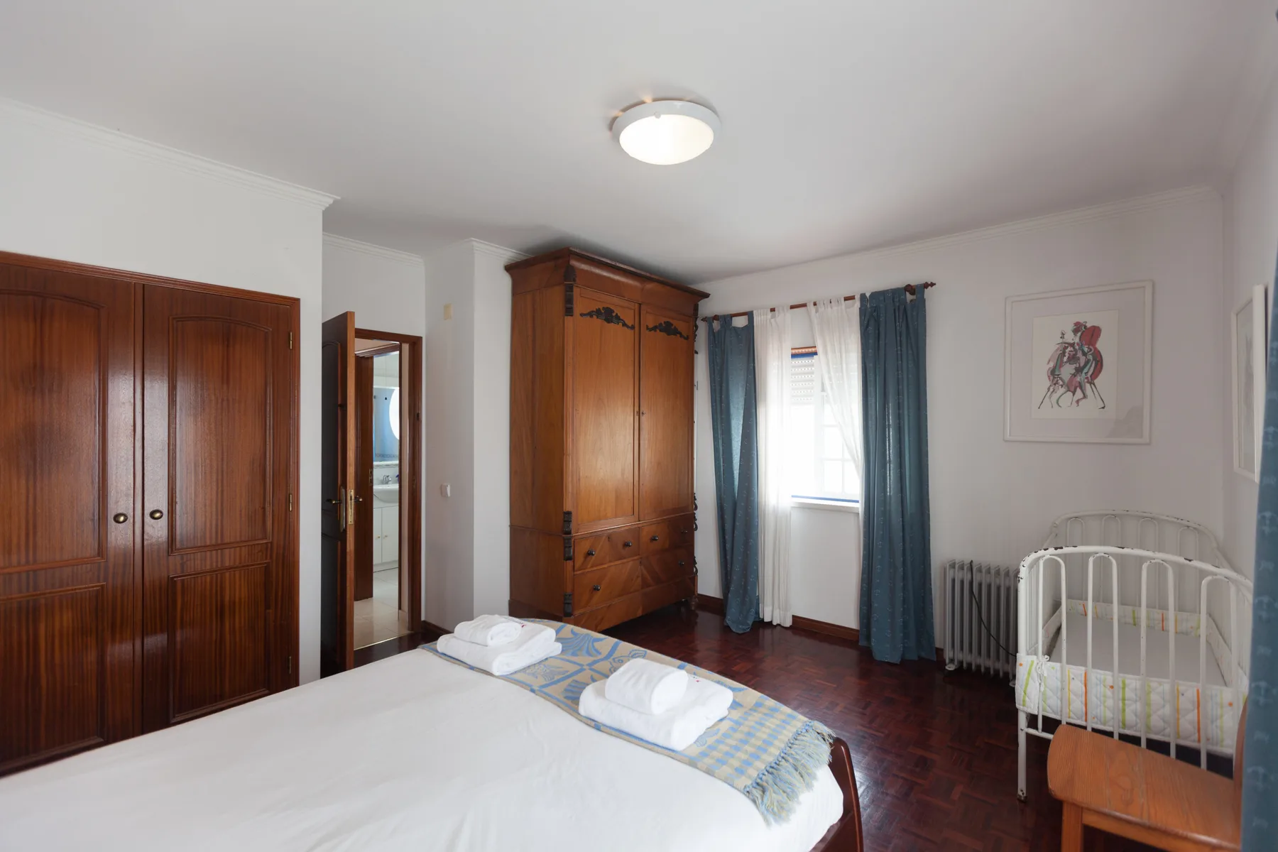 A bedroom with a large bed, wardrobes, and a white crib.