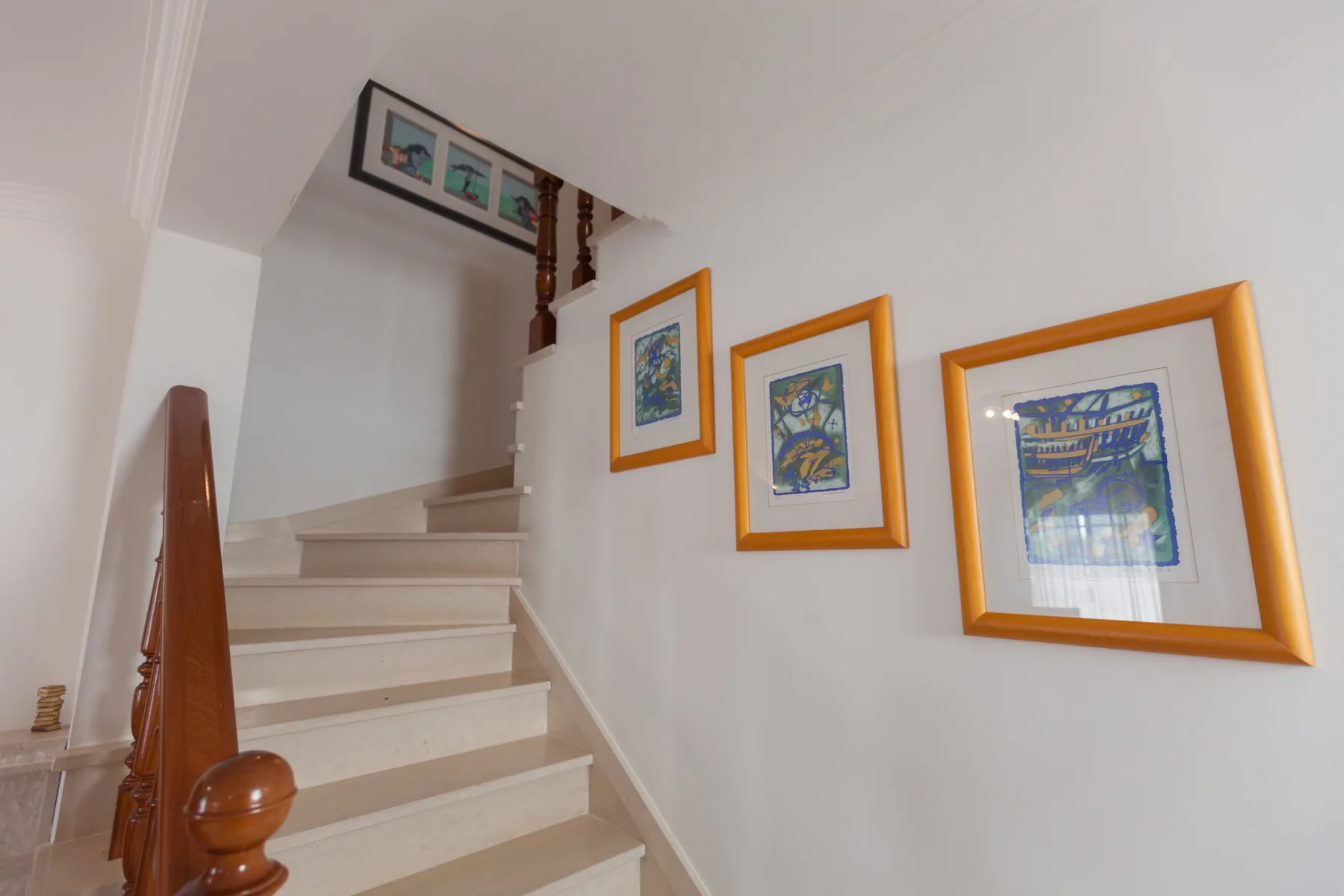 Una escalera interior sube junto a cuadros enmarcados en la pared.