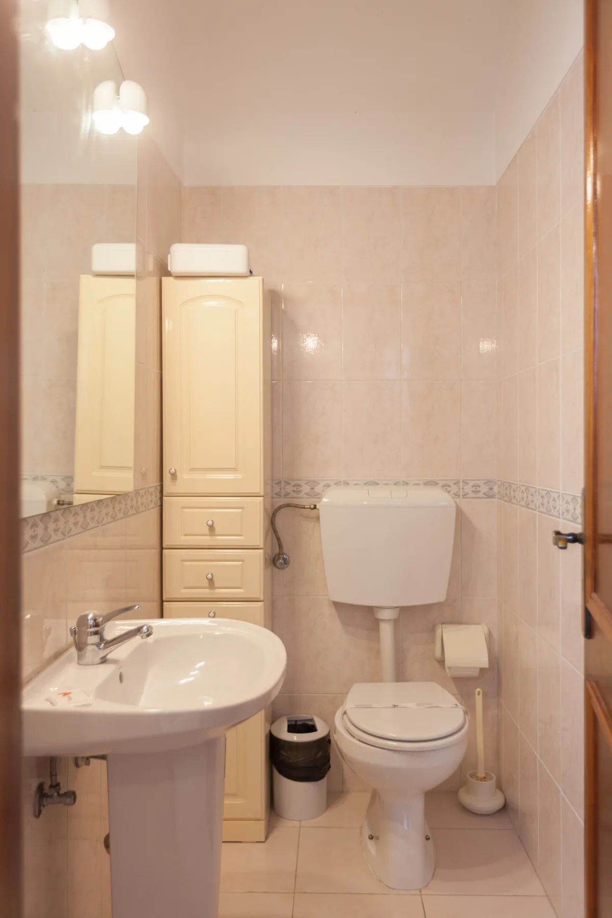 A tiled bathroom with a sink, toilet, and tall storage cabinet.