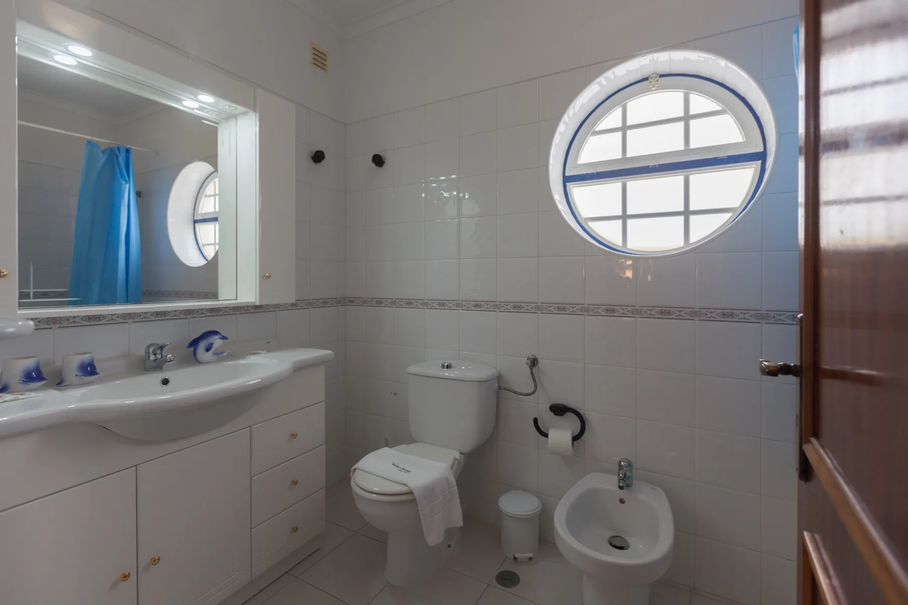 A tiled bathroom with a sink, toilet, and round window.