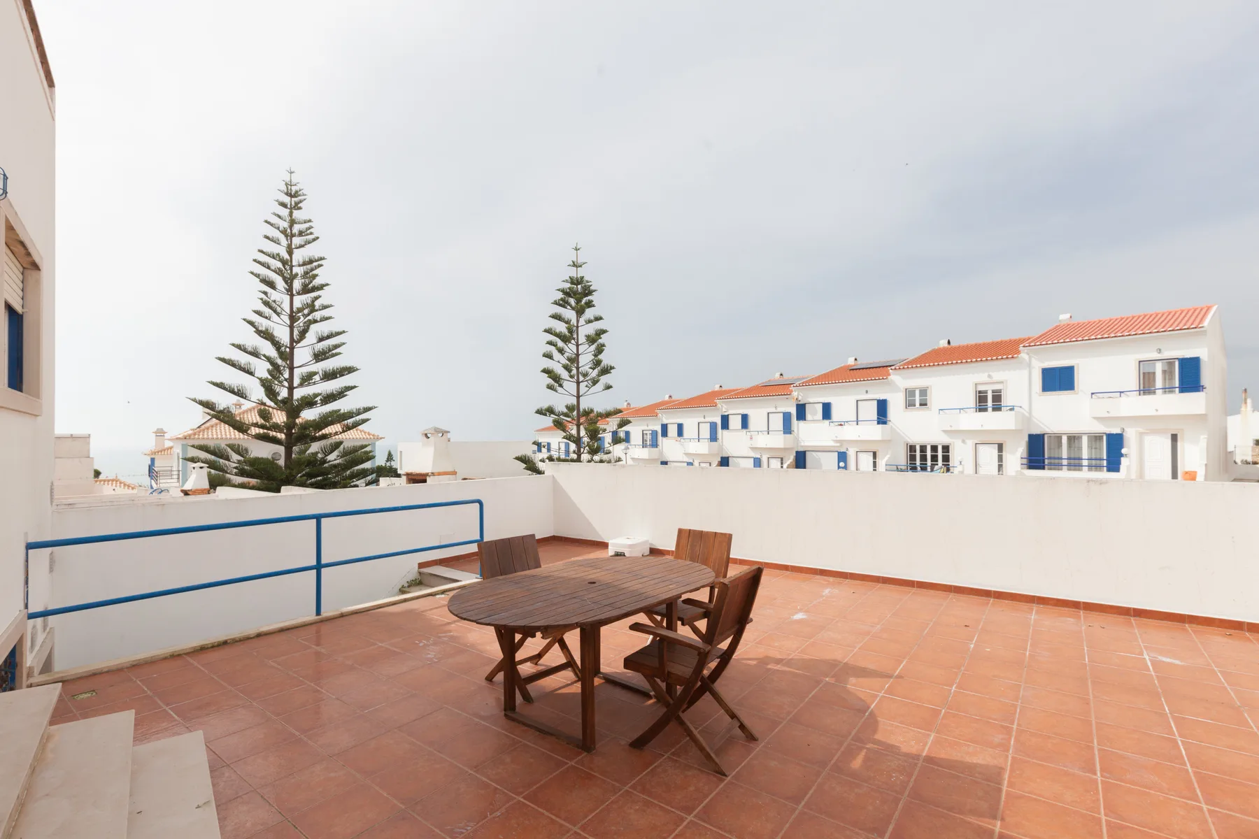 A tiled terrace with outdoor seating overlooks nearby buildings and trees.