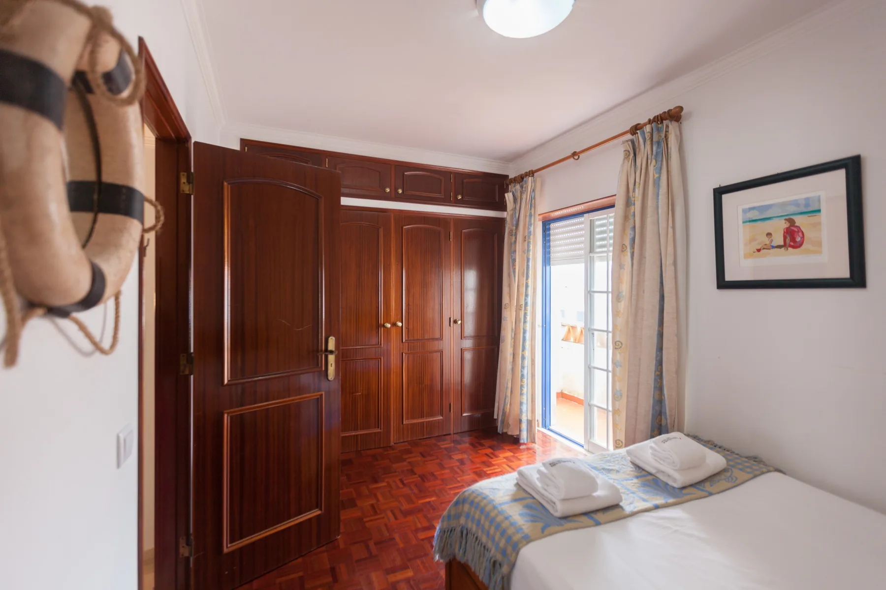 A bedroom with a bed beside wooden wardrobes and a bright window.
