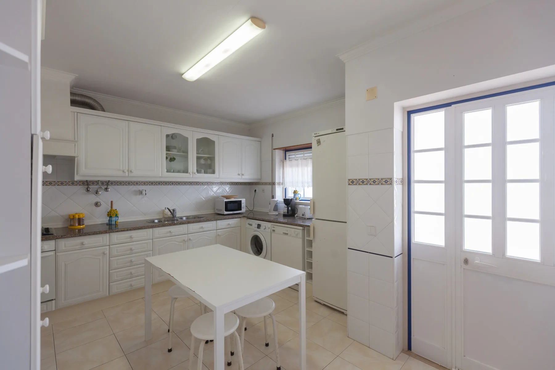 A bright kitchen with white cabinets, appliances, and a central table.