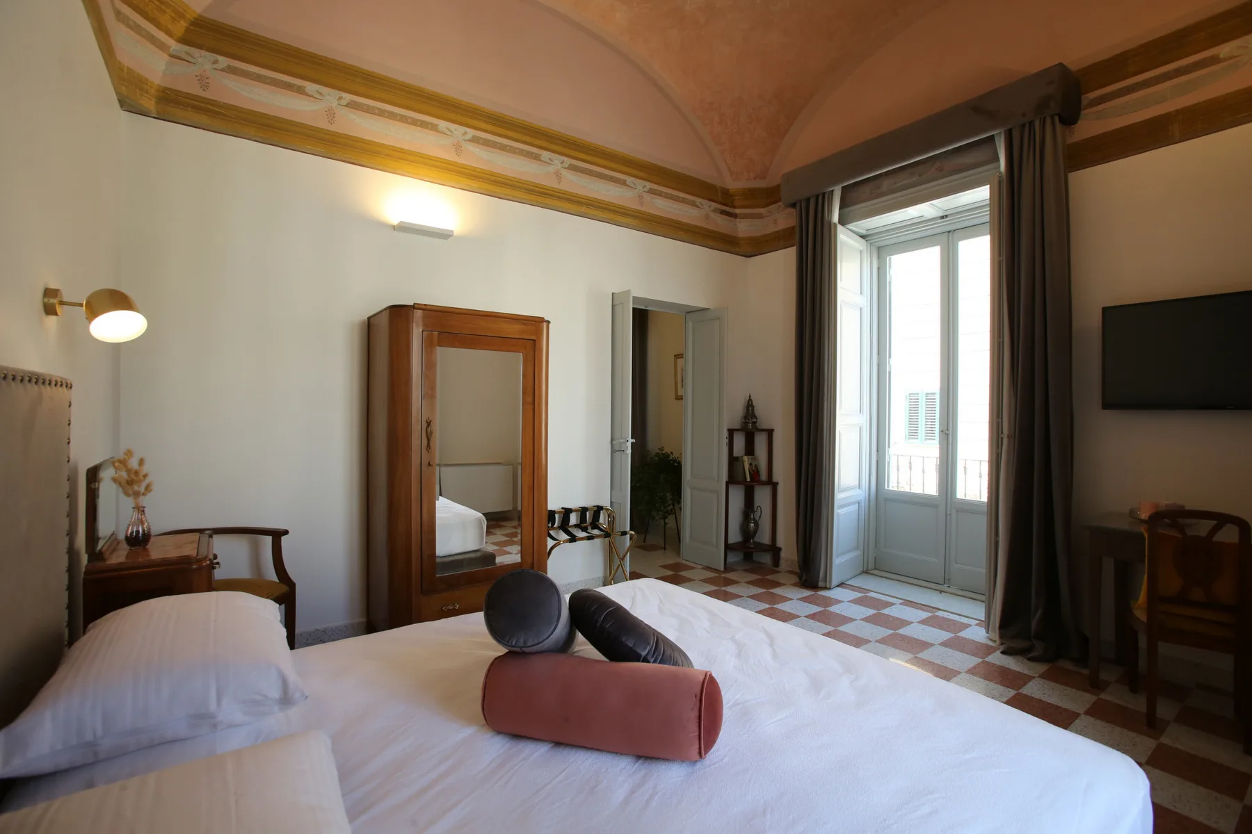 A bedroom with two beds, a wardrobe, and a tall window.
