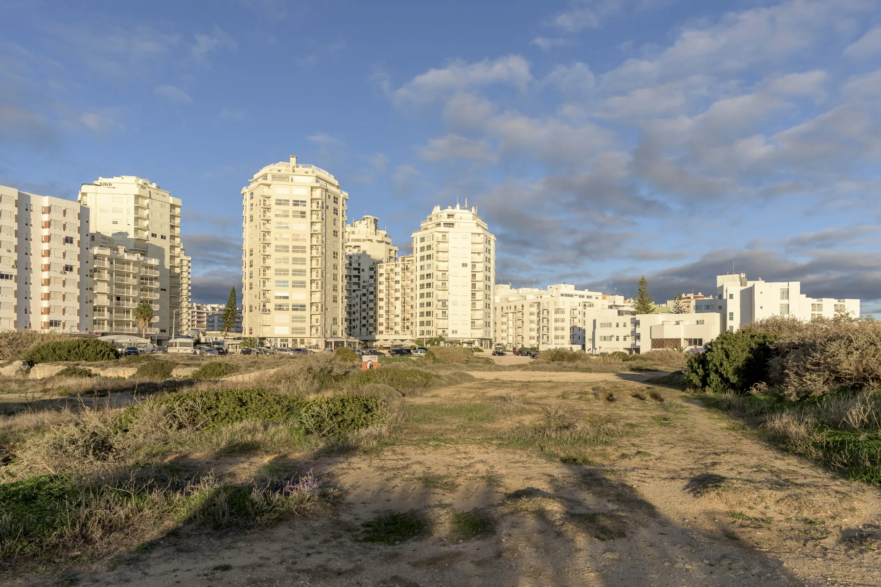 High-rise apartment buildings stand beyond a grassy open area under a blue sky.