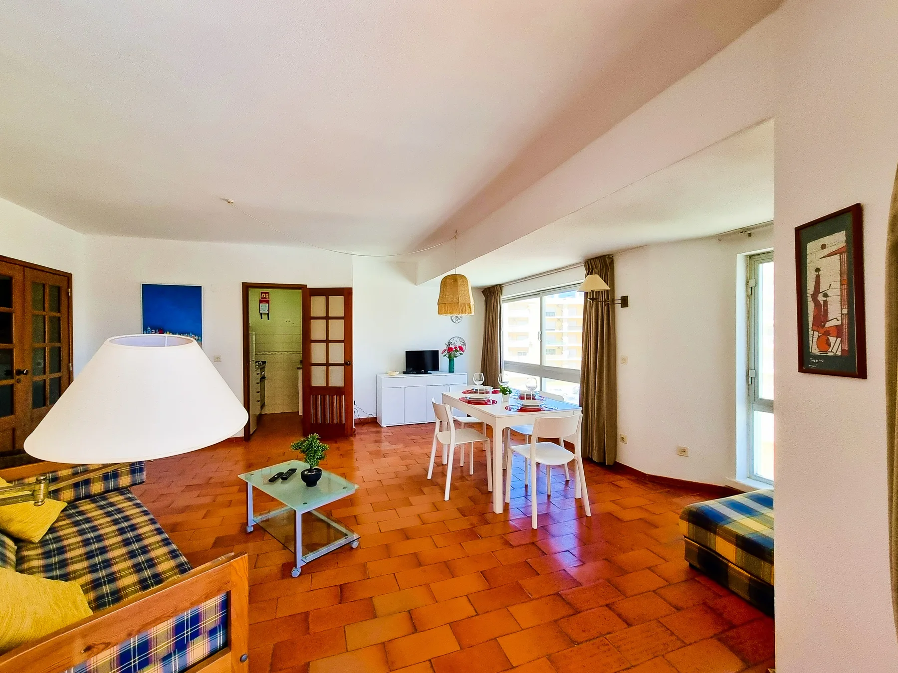 Una sala de estar y comedor con asientos, una mesa y grandes ventanas.