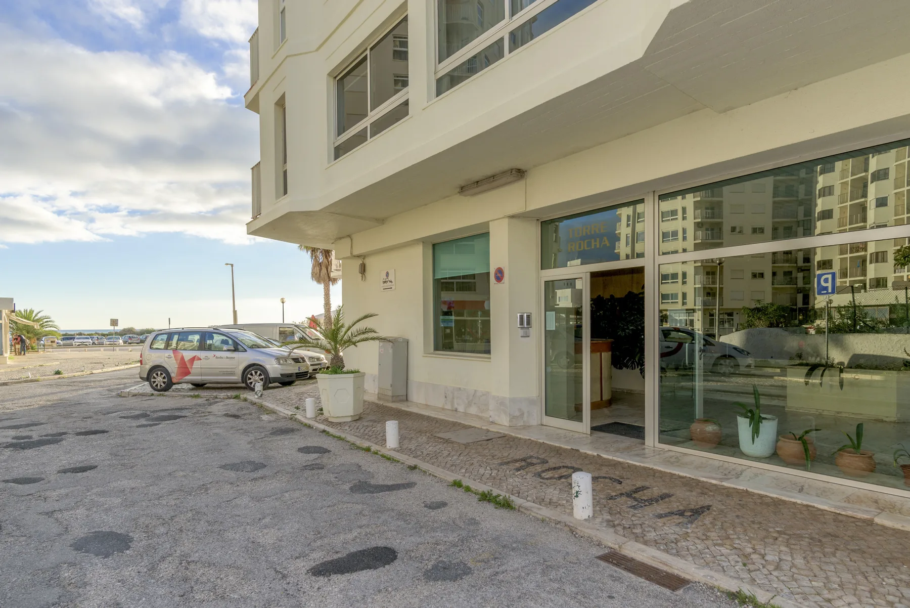 Entrada de un edificio moderno con amplios ventanales junto a una calle pavimentada.