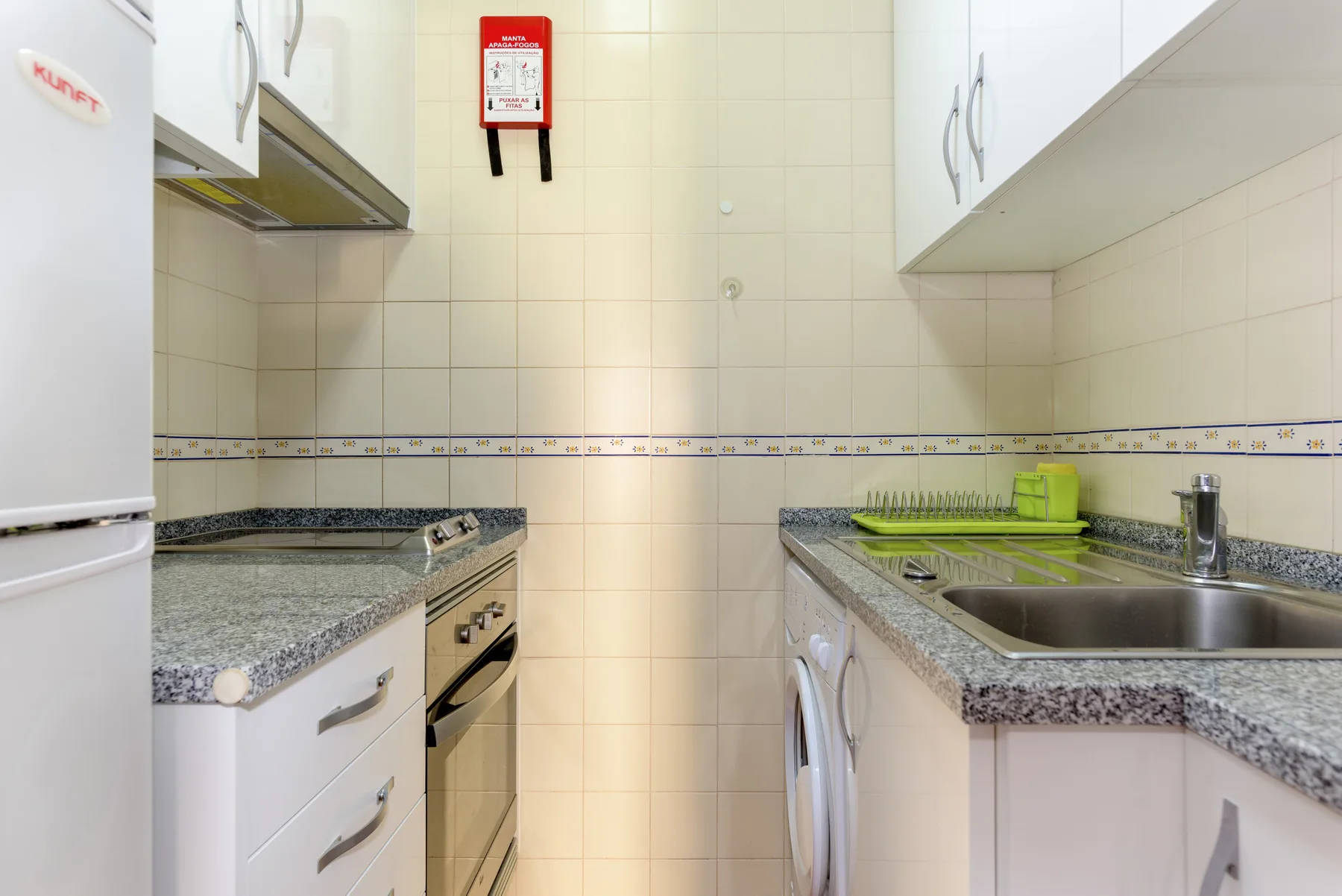 A compact kitchen with tiled walls, counters, and a sink.