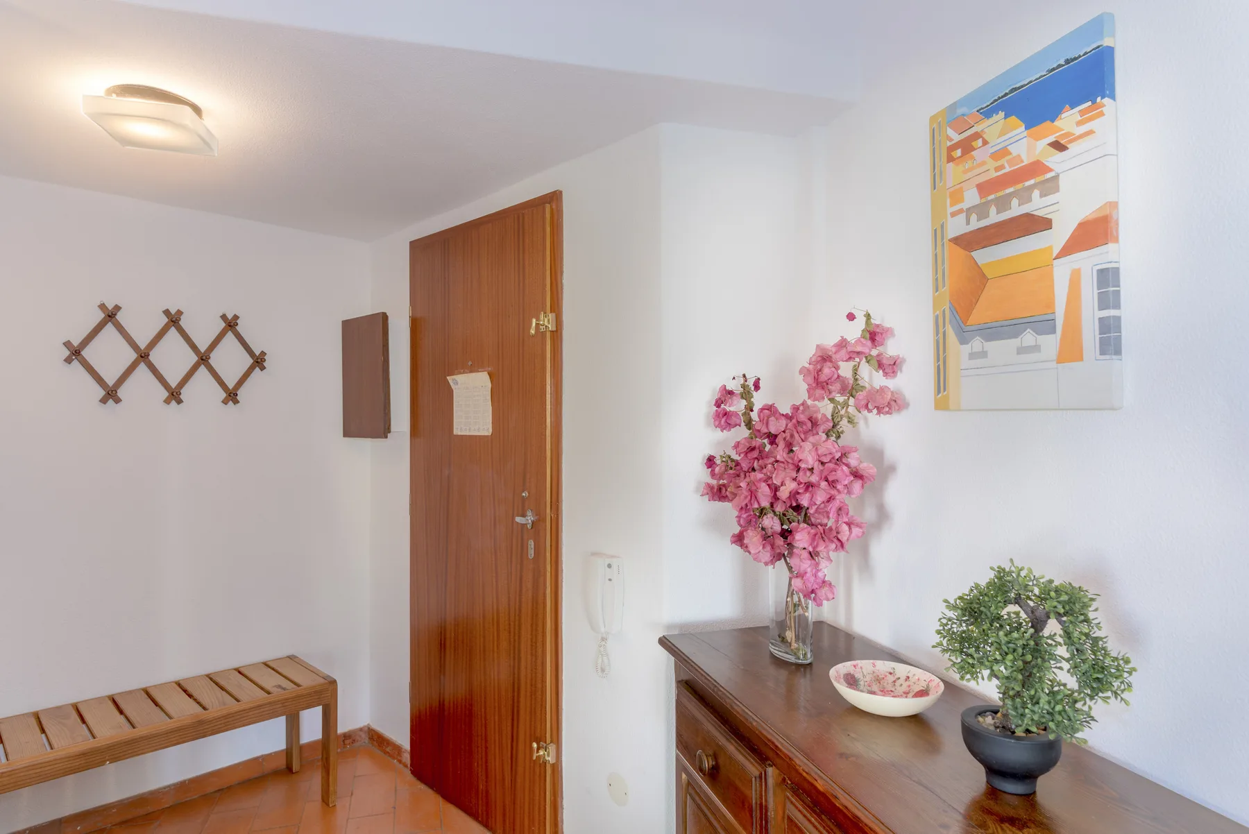 Una entrada de apartamento con una puerta de madera, una consola y plantas decorativas.