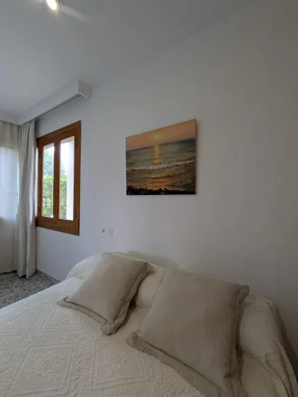 Un dormitorio con una cama bien tendida bajo un paisaje marino enmarcado.