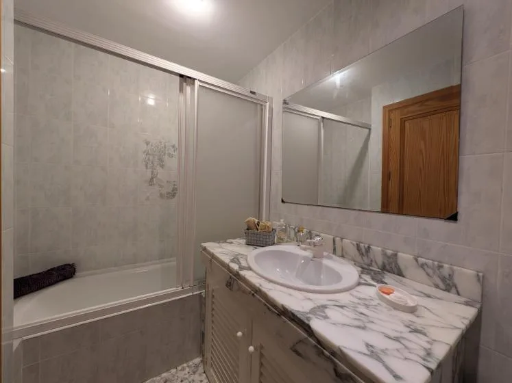 Un baño alicatado con bañera, mampara de ducha y lavabo con mueble.