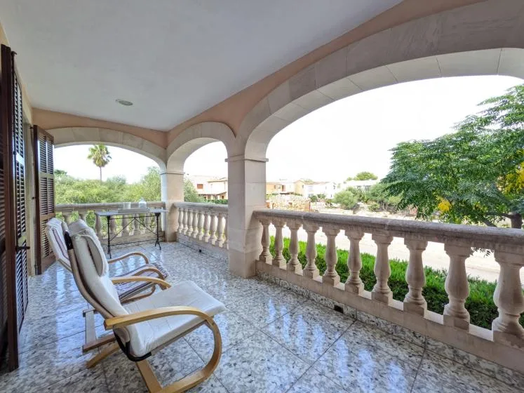 Una terraza cubierta con asientos acolchados da a zonas verdes y casas cercanas.
