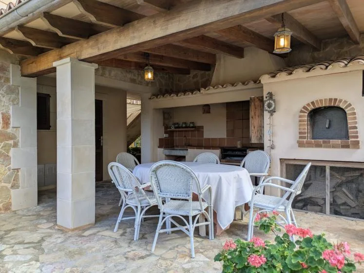 A covered outdoor dining area with a table, seating, and a built-in barbecue.