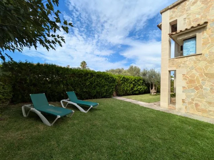 A grassy outdoor seating area beside a stone building and tall hedges.